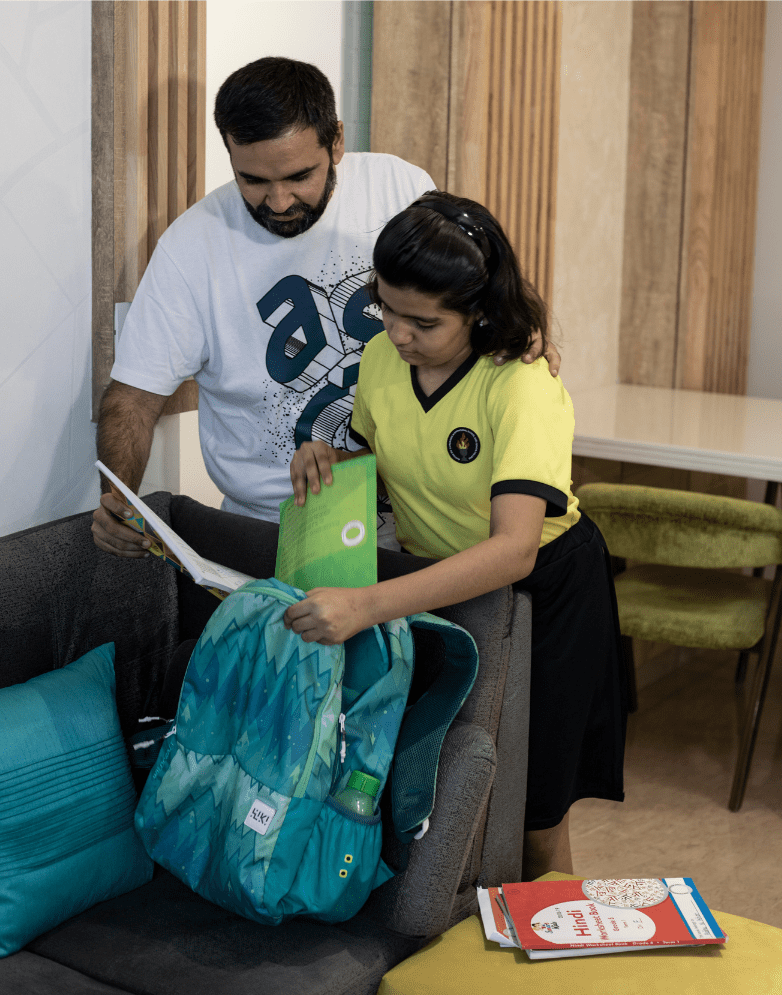 A Muslim father helps his elementary school daughter pack her backpack.