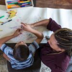 An elementary age boy with Down Syndrome coloring with female therapist during play therapy session.