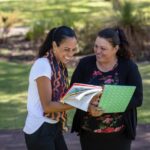 A high school student smiles with her teacher while reviewing school work together. 