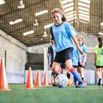 A middle school student runs with a soccer ball around cones during team practice.