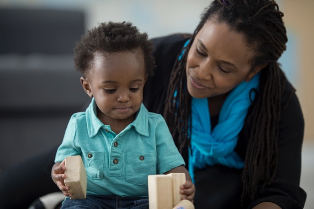 A black mother is spending quality time with her toddler son at home. They are laughing and playing together.