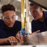 A young black student learns how to use a saw with a mentor during Carpenter Training