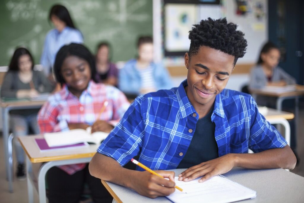 Smiling black high school student writes during class.