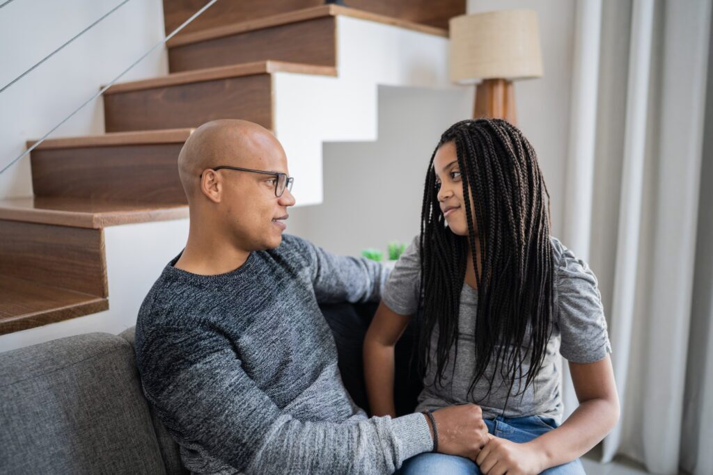 Father and daughter sitting on the couch in the living room and talking at home