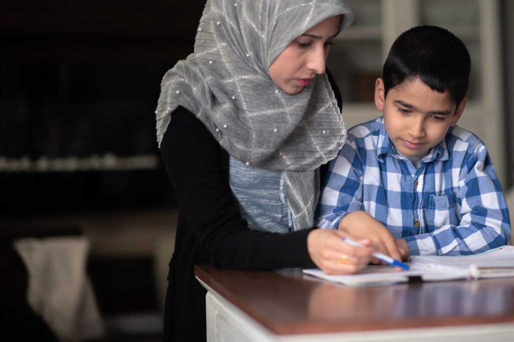 A middle eastern woman is helping her son with his school work in their living room at home.