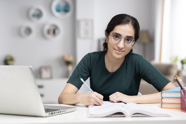 An Asian high school student works on her homework with a laptop open at home.