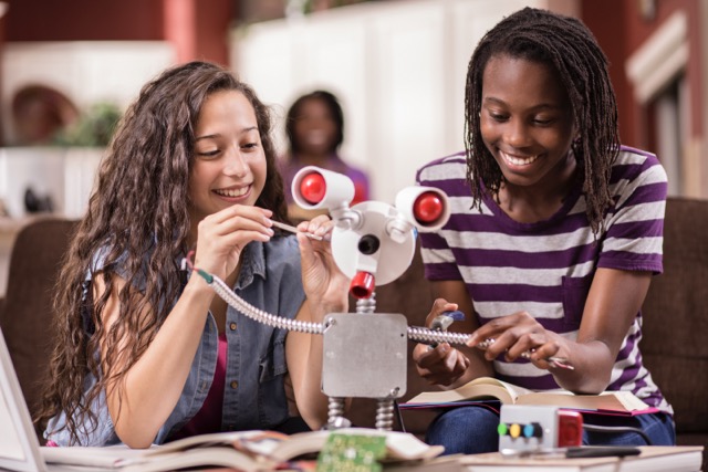 Multi-ethnic team of high school age girls work on engineering science project at home.