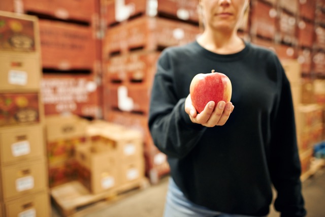 A cropped image of a woman holding an apple in an agricultural warehouse