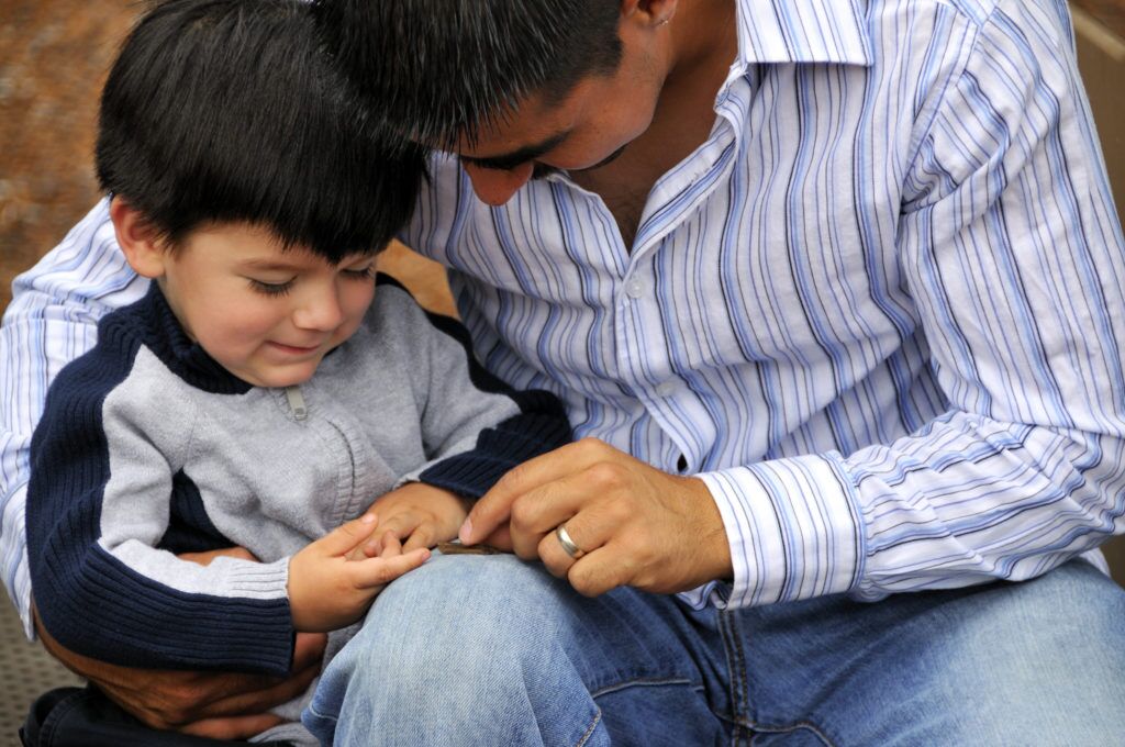 A young father hugs his toddler son as they examine the toddler