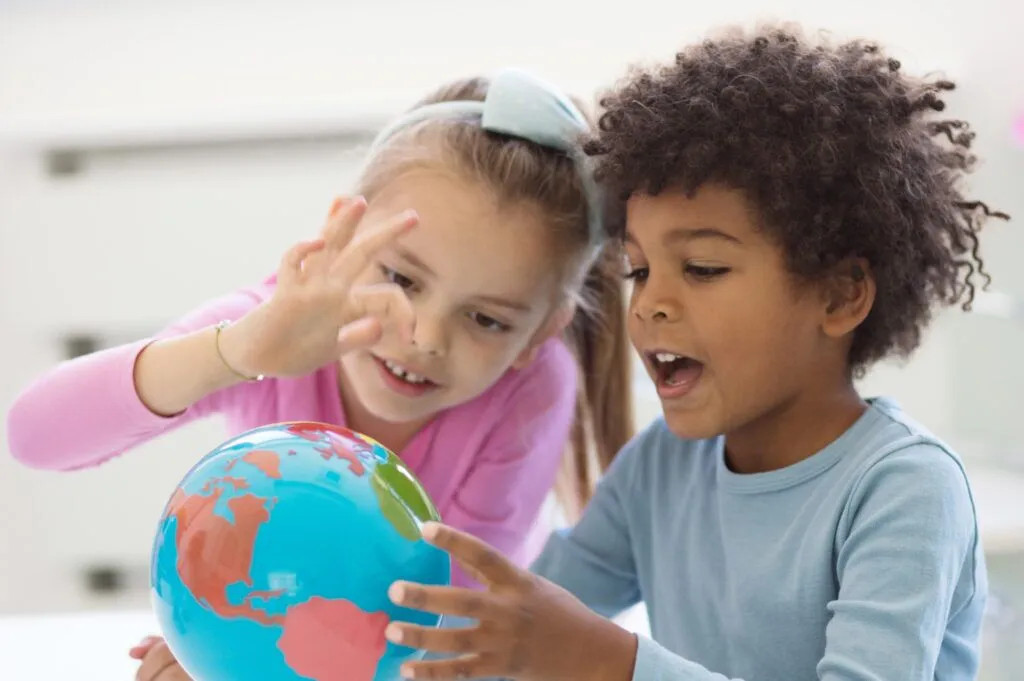 Two preschool students examine a toy globe while smiling.