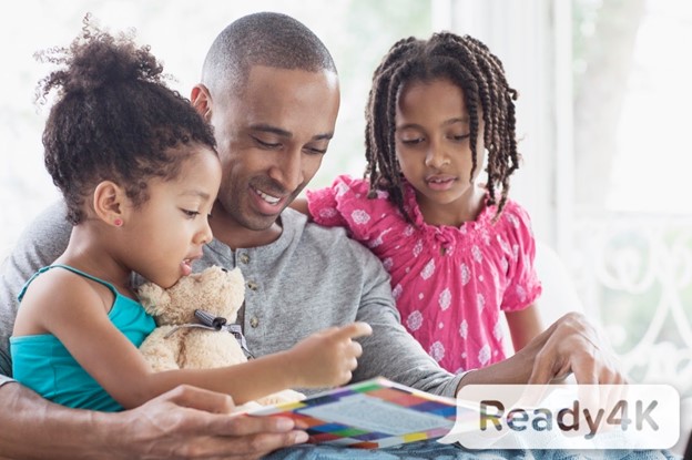 A black father reads to his two young daughters; all are smiling; ParentPowered logo is watermarked on image. 