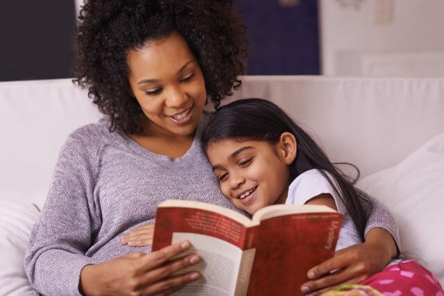 A mother reads with her elementary school daughter on the couch at home.
