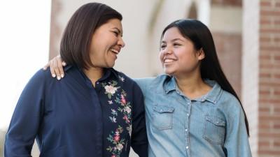 Latin mother and her pre-teen daughter smile together; daughter has her arm around her mother.