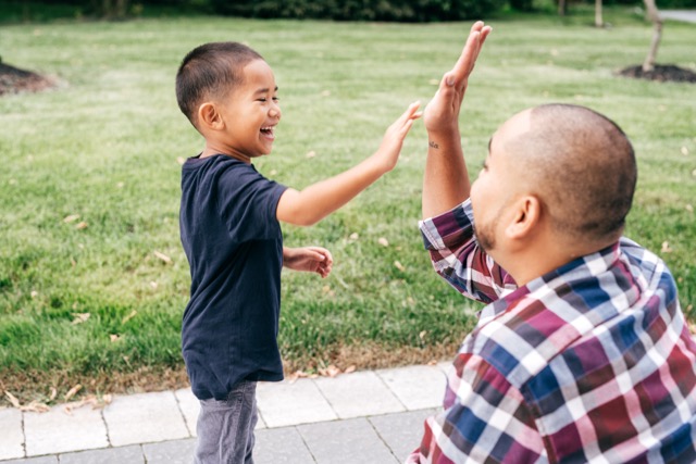 A mature Asian father gives his young son a high-five during a walk through the park.