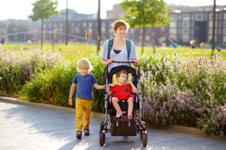 A Caucasian mother walks her toddler son and daughter with cerebral palsy through their local community park.