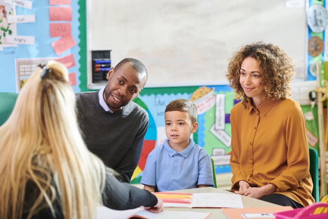 A multiethnic family meets with their young son's kindergarten teacher in the classroom.