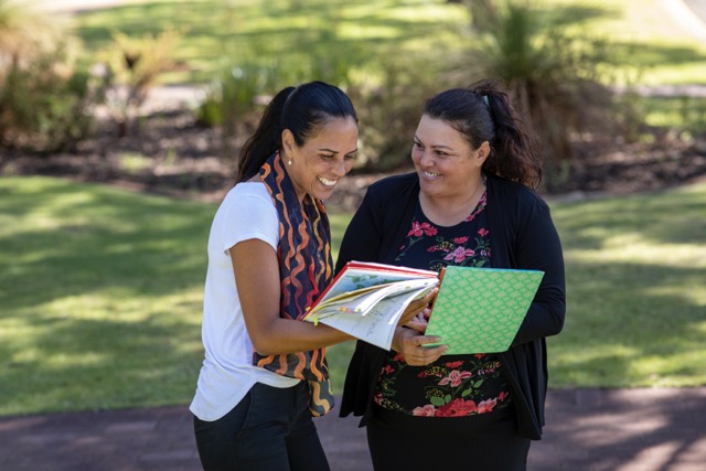 A teenage Aboriginal student smiles and speaks with her teacher outdoors in the sun in Australia.