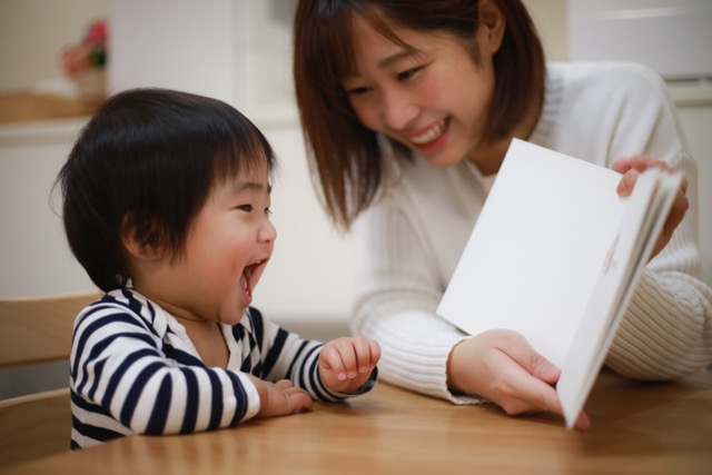 An Asian mother smiles as she shows her delighted infant son a picture book.