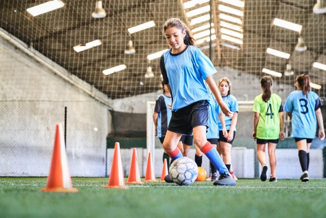 Young girl leads a soccer ball between cones on sports court at school.