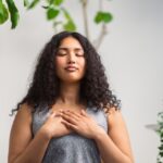 A multiracial mother holds her hands on her chest and does a deep breathing exercise. 