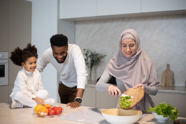 A Muslim family smiles as they prepare a meal together in the kitchen.
