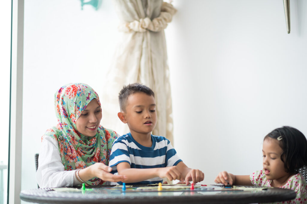 A Muslim woman plays a board game with her two young children at home.