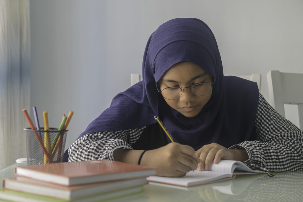 An Asian preteen girl does her homework on dining table at home.