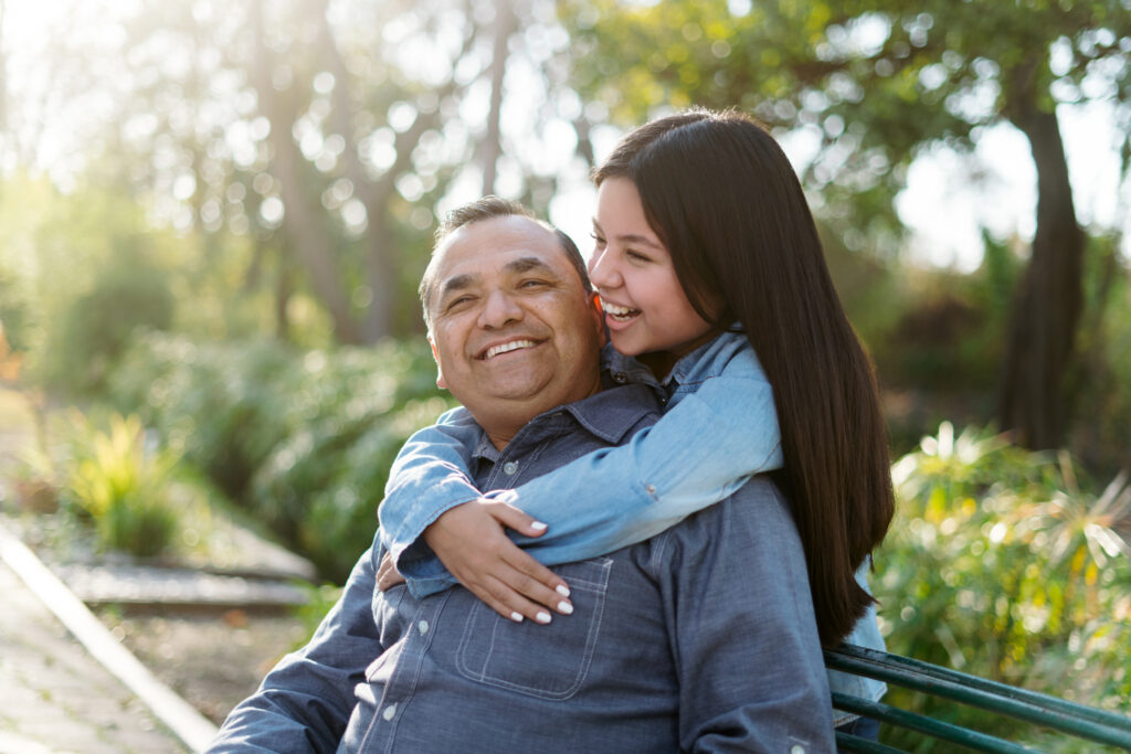 Smiling latino father with his daughter sitting on a park bench.