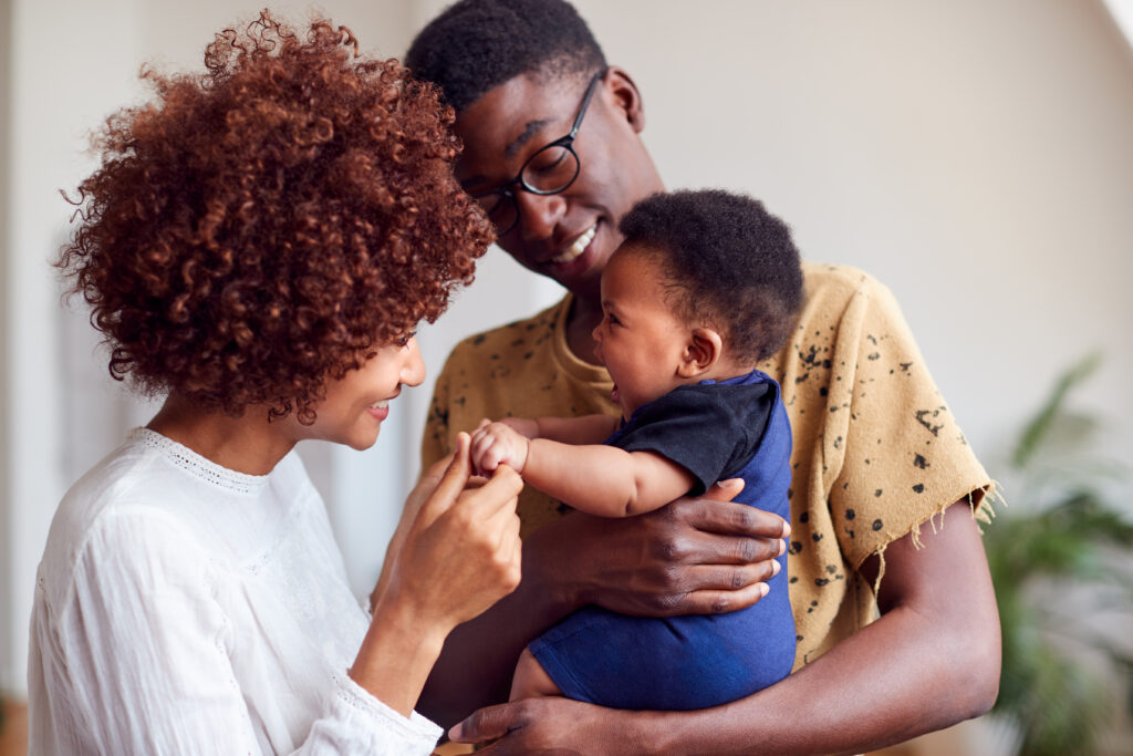 A young black mother and father smile as they hold their smiling baby boy.