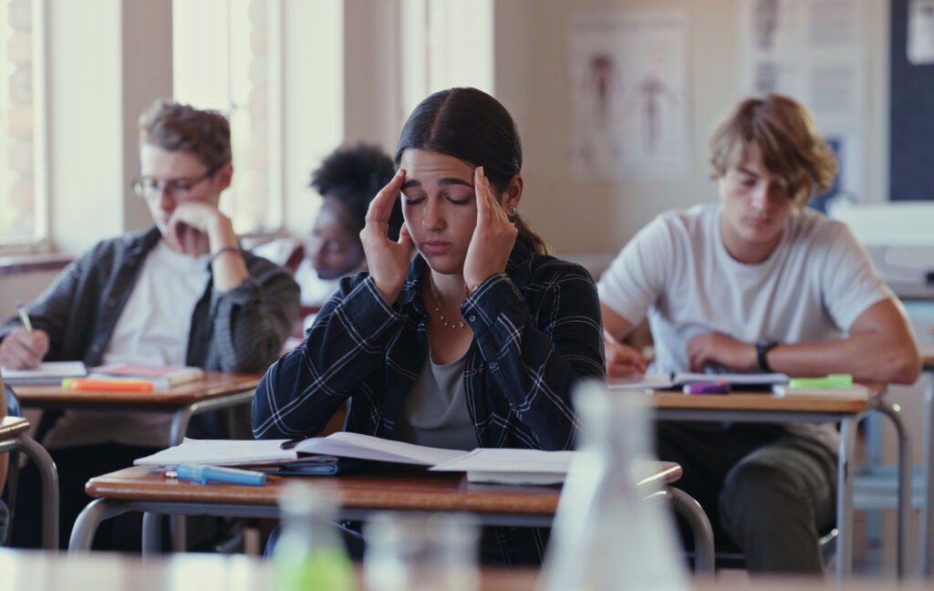 A middle school student holds her head in her hands in class, struggling with her school work.