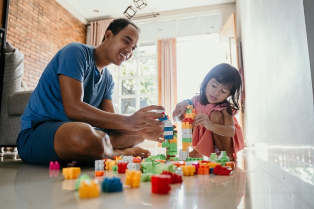 An Asian father helps his preK daughter practice math skills with building blocks at home.