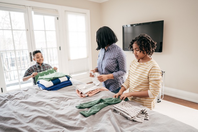 A black mother has help from her teen and pre-teen children folding laundry.