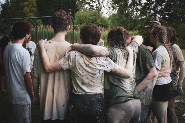 A group of teenagers form a circle and put arms around each other shoulders after a camp activity.