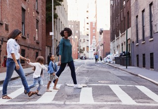 Two mothers with two daughters crossing the road while smiling.