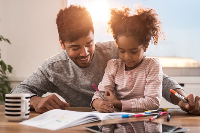 A smiling African American father and daughter coloring on a piece of paper while spending their free time at home.
