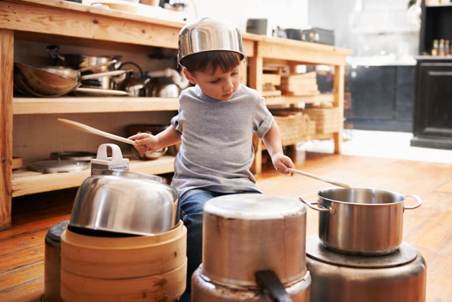 A preschool Caucasian boy plays drums on pots and pans at home.