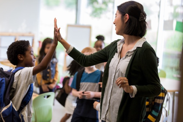 Cheerful Hispanic elementary school teacher gives a high five to a student before class.